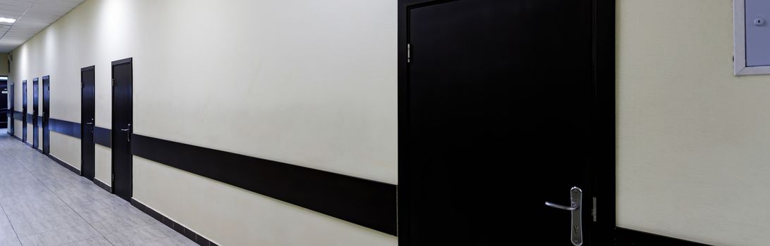 empty corridor in the modern office building. There are many brown doors along a very long corridor with beige walls.