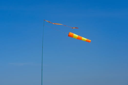 flagpole with wind indicator on a background of blue sky on a windy day