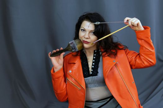 Portrait of a beautiful fashionable middle-aged woman in a bright orange leather jacket, posing on a dark gray background