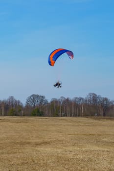 the paraglider begins to take off over the field on a sunny spring day
