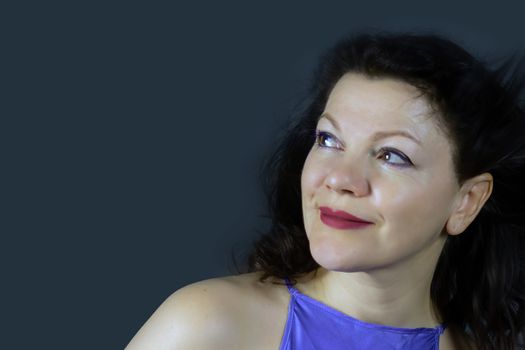 Portrait of a beautiful fashionable middle-aged woman with long dark hair, posing on a dark gray background. The concept of preserving youth at any age.