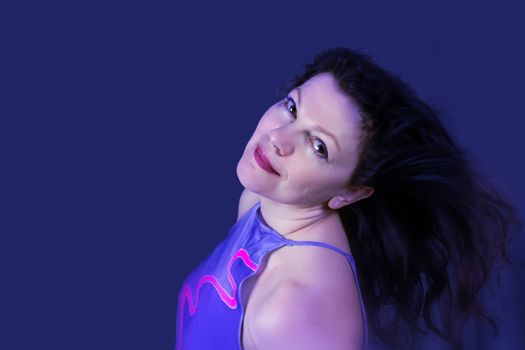 Portrait of a beautiful fashionable middle-aged woman with long dark hair, posing on a dark blue background. The concept of preserving youth at any age.