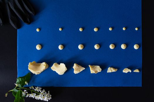 Top view of pieces of white milk chocolate spread out on a blue and black background and a sprig of white spring flowers.