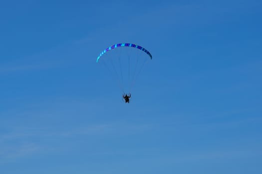 paraglider with a blue parachute flies against a cloudless blue sky