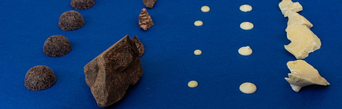 Pieces of natural dark chocolate and white chocolate on a blue background