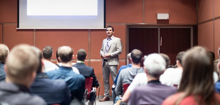 Speaker giving a talk in conference hall at business meeting event. Rear view of unrecognizable people in audience at the conference hall. Business and entrepreneurship concept.