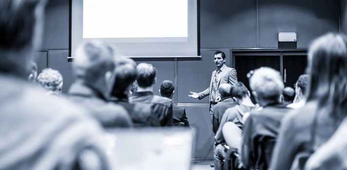 Speaker giving a talk in conference hall at business meeting event. Rear view of unrecognizable people in audience at the conference hall. Business and entrepreneurship concept.