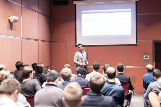 Speaker giving a talk in conference hall at business meeting event. Rear view of unrecognizable people in audience at the conference hall. Business and entrepreneurship concept.