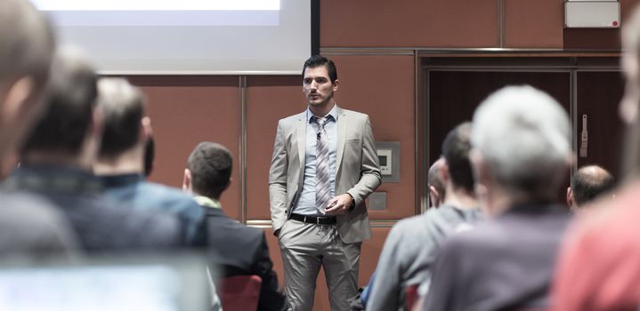 Speaker giving a talk in conference hall at business meeting event. Rear view of unrecognizable people in audience at the conference hall. Business and entrepreneurship concept.