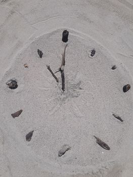 A clock face made on the beach in sand with sticks for hands and stones for hours