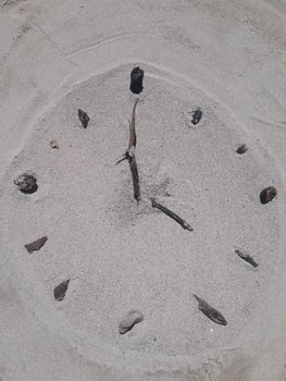 A clock face made on the beach in sand with sticks for hands and stones for hours