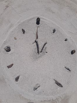 A clock face made on the beach in sand with sticks for hands and stones for hours