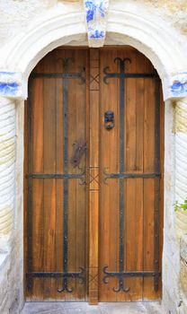 Antique wooden antique doors with wrought iron bars and crossbeams stand in an arched stone passage with stone columns.