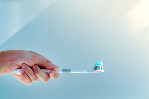 Woman hand holding toothbrush with toothpaste applied on. Closeup of  white toothbrush with blue tooth paste