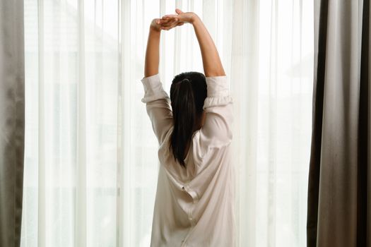 Woman stretching in bedroom after wake up, back view