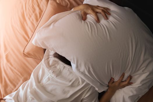 Sleepy woman hide under the pillow hates waking up early in the morning