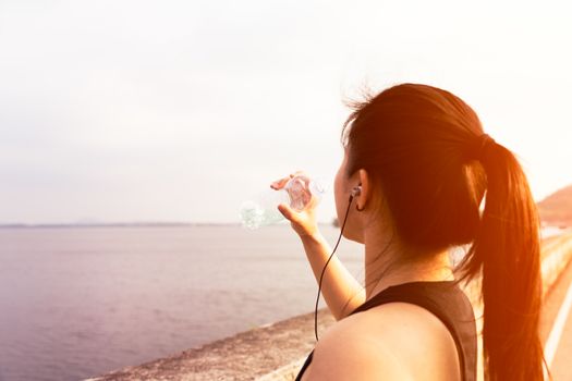 Sport woman standing on the bay and drinking water after running
