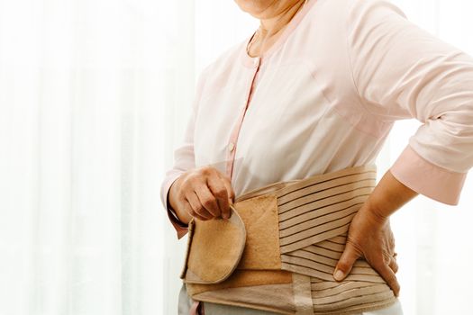 back pain, senior woman wearing back support belt on white background