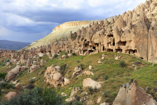 Quarter of old antique residential caves on the background of the conical ridges of Cappadocia and the blue cloudy sky