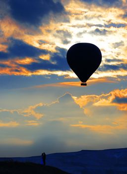 Silhouette of a couple in love on the horizon and a balloon against the background of the morning sky and fiery red clouds