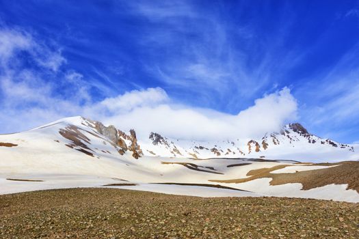 The snowy top of Mount Erciyis in central Turkey is shrouded in a white cloud against a bright blue sky on a sunny spring day