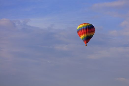 A motley multicolored beautiful balloon raises the tourist's basket to the blue sky under the sun rays among the clouds.