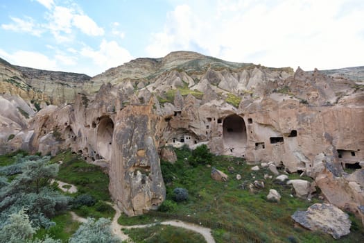 Old ancient city of red sandstone under the open blue sky, huge residential caves in the valley on the background of the conical ridges of Cappadocia