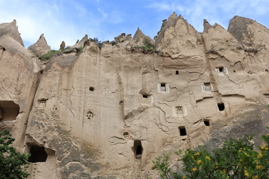 Multi-level caves in the old ancient city of red sandstone under the open blue sky in the valley of Cappadocia
