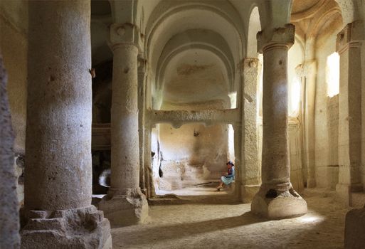 A young beautiful girl is in the pillared hall of an old, antique, underground church carved out of a sandstone cliff in Cappadocia