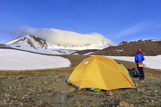 The tent of tourists is located at the foot of Mount Erciyes, a young tourist girl has her back turned and looks at the top of the mountain, on the left side of the copy space.