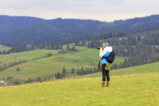 A young girl photographer shoots the landscape of the Carpathian slopes on a fresh spring morning