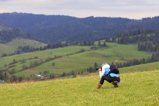 A young girl photographer half crouching shoots the landscape of the Carpathian slopes on a fresh spring morning