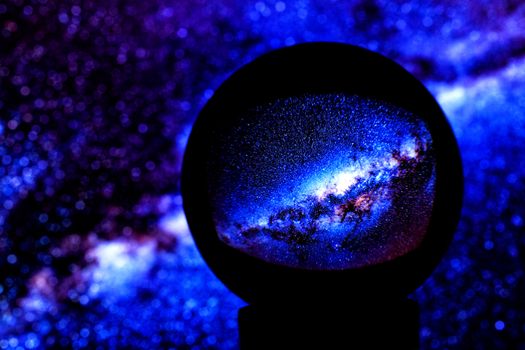 Stars of the Milky Way galaxy are reflected in a crystal ball on a blue blurred background, on the left side of the copy space.