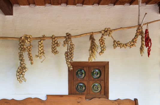 View of the terrace of an old Ukrainian rural hut with an antique window and pigtails of onion, corn and pepper drying on a wooden pole.