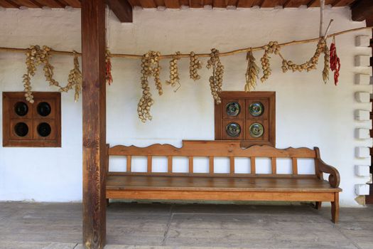 wooden terrace of an old country Ukrainian house with an oak wooden bench, antique windows and pigtails of dry corn, onions and peppers