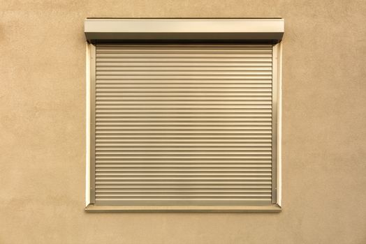 Light brown metal blinds on the window of the facade of the house.