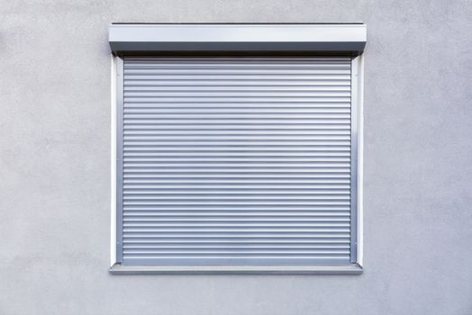 Light gray metal blinds on the windows of the facade of the house.