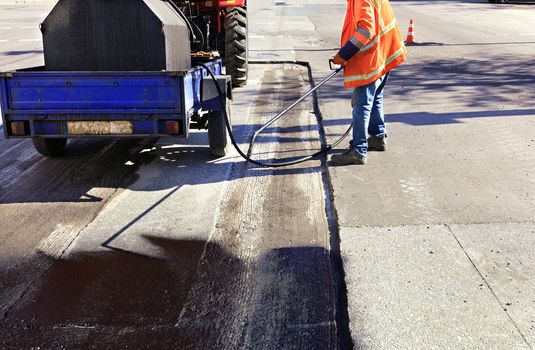 The road maintenance worker sprays the bitumen mixture onto the cleaned area for better adhesion to the new asphalt