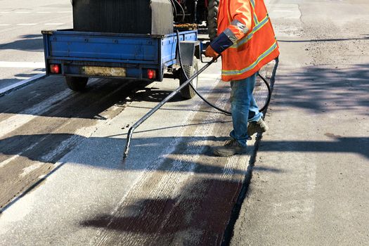 The road maintenance worker sprays the bitumen mixture onto the cleaned area for better adhesion to the new asphalt