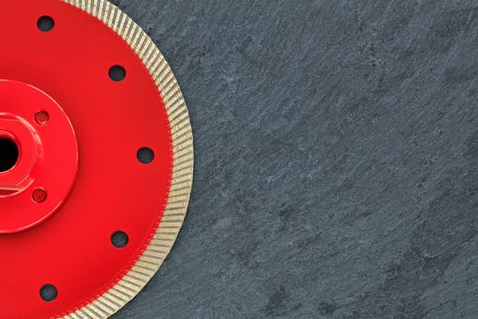 Half of the diamond cutting wheel is red with a threaded nut, on the right side is a copy space on a gray granite background close-up.