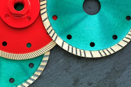 Several diamond cutting wheels of red and emerald color are located on top of each other against the background of gray granite close-up.