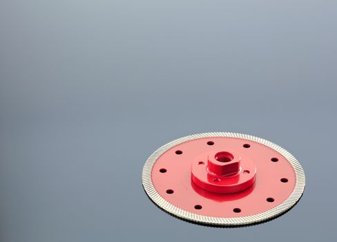 Diamond cutting wheel is red with a threaded nut, on the left side is a copy space on the mirror surface of a gray background with a slight gradient.