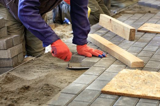 The worker levels the platform for laying paving slabs with the help of a trowel and wooden bars, aligning it to the level of the tensioned thread.