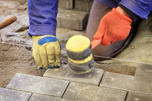 The worker lay the paving slab with special hammers, leveling it according to the level of the tensioned thread