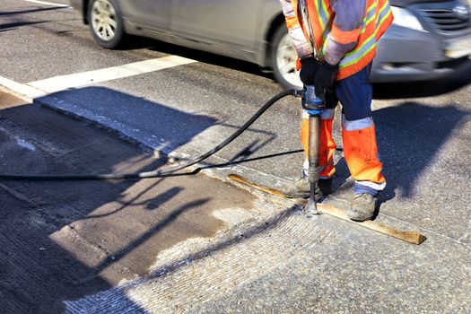 A road maintenance worker removes old asphalt on the roadway with a jackhammer into an excavator during road construction.