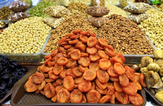 Slides of dried apricots close-up, prunes, figs on the background of various nuts in the blur are sold on the shelves of the eastern market.