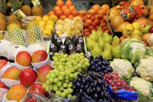 Bright background of fresh fruits, green black red berries of grapes, mango, pears, apples, pineapple, melon lie in the trays in the market and attract attention.