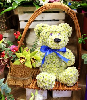 Close-up of a beautiful composition of a toy bear from small blooming chrysanthemums in a wicker basket frame with a large orchid flower.
