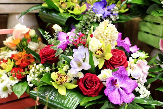 Closeup of a beautiful bouquet of fresh red, white roses and different orchids in bloom against other flowers in blur