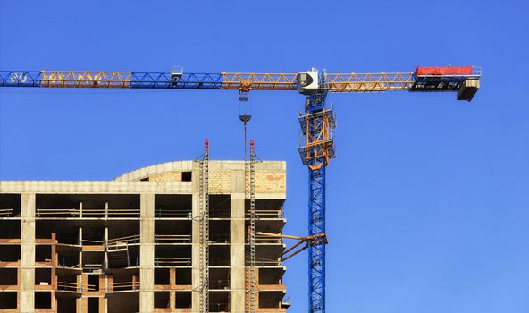 A fragment of the facade of a house under construction, a modern building is being built, an arrow of a tower crane is directed parallel to the roof against a blue cloudless sky.